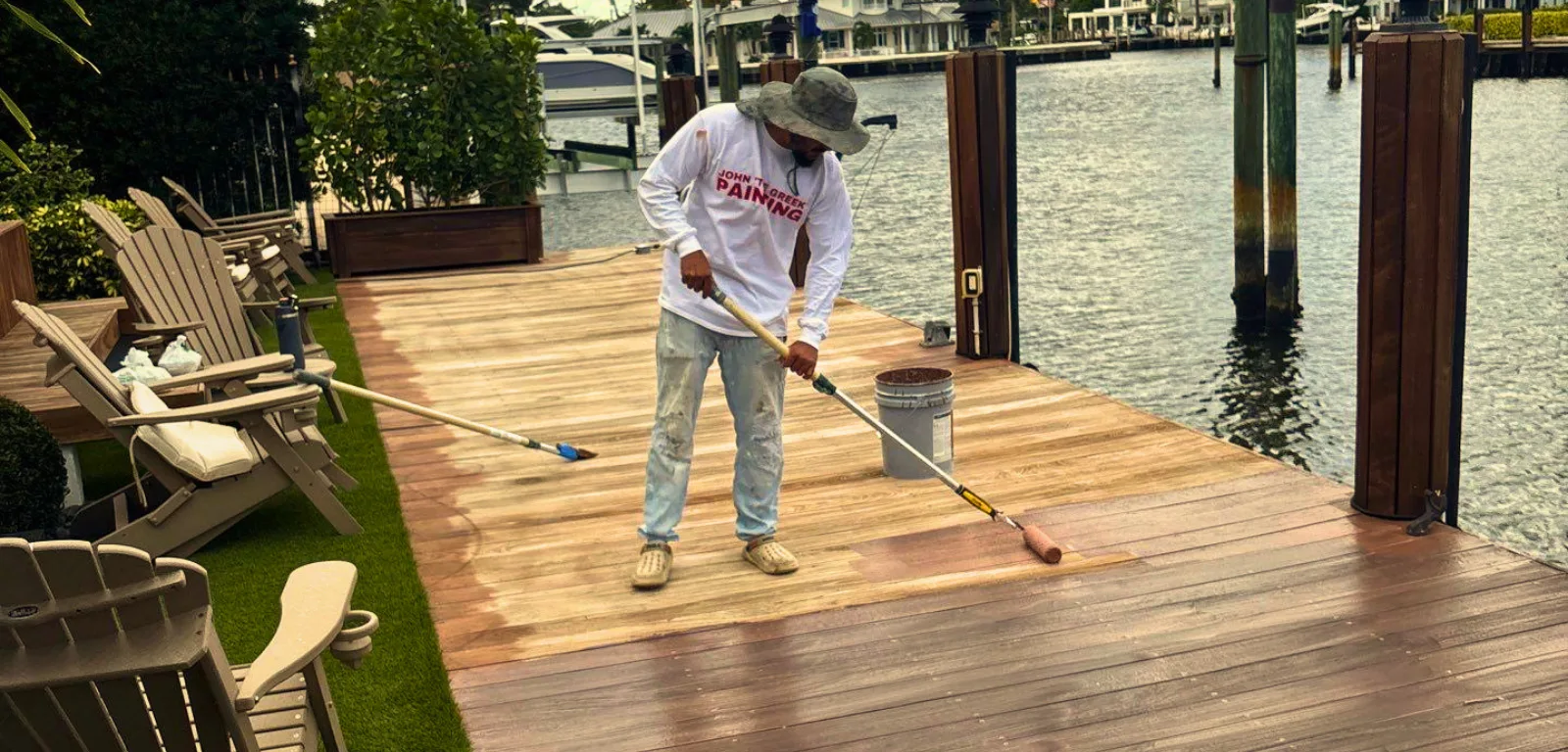 John The Greek Painting technician applying penetrating oil with a roller to an Ipe wood dock at a waterfront South Florida property